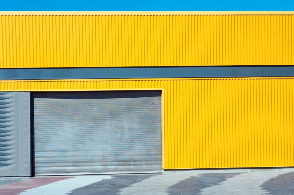 Modern garage door with a sleek, gray finish against a vibrant yellow wall, emphasizing contemporary architectural design.